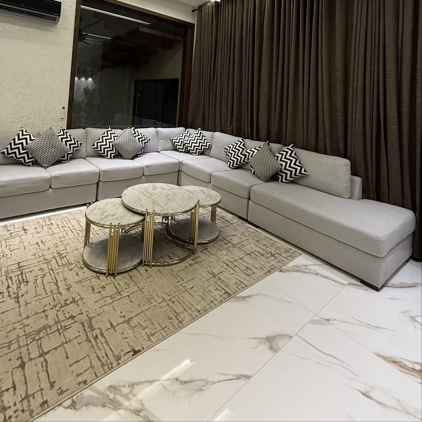 A modern and elegant living room featuring a grey L-shaped sofa and marble-top coffee tables.