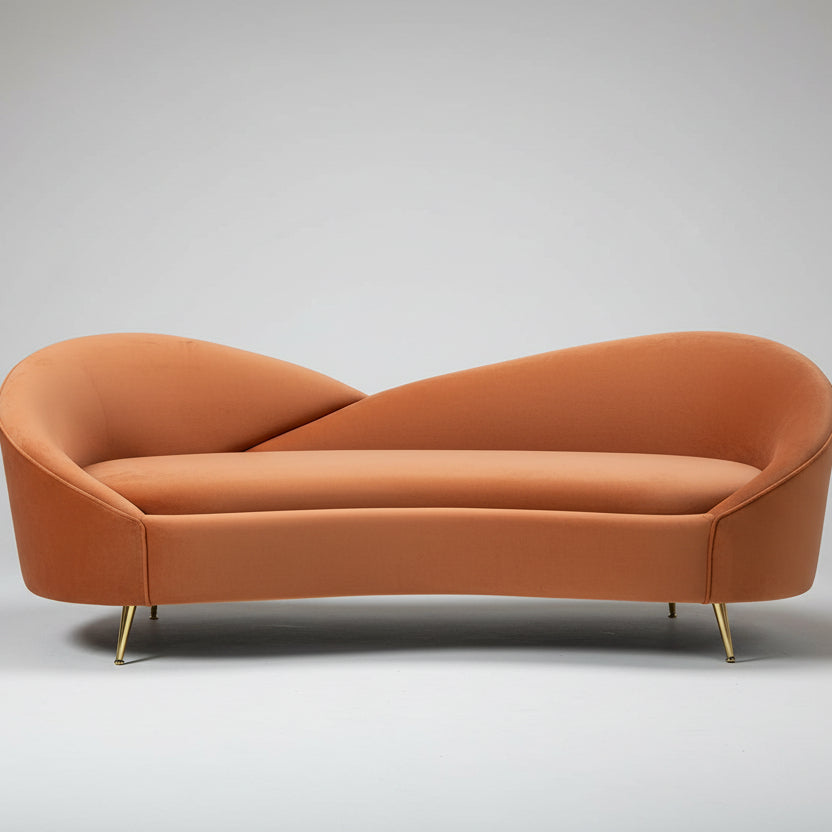 A luxurious terracotta velvet sofa with a unique comma shape and slender gold legs, set in a workshop or production area.