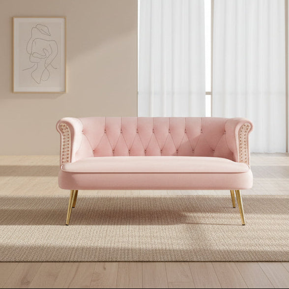 A stylish pink velvet tufted loveseat with gold nailhead trim and gold metallic legs,