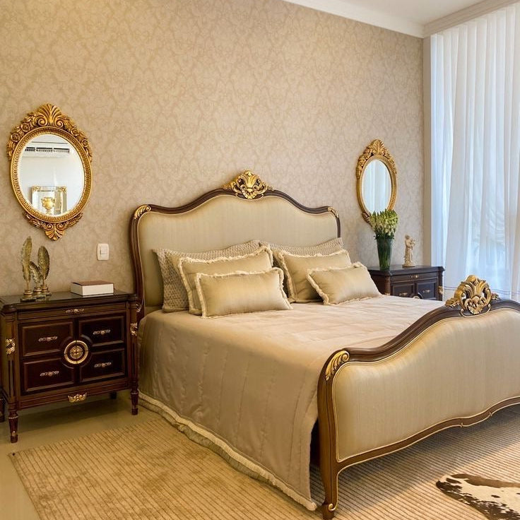 A lavish Louis style bed with a dark wood frame and ornate gold carvings on the headboard and footboard, upholstered in a light beige fabric.