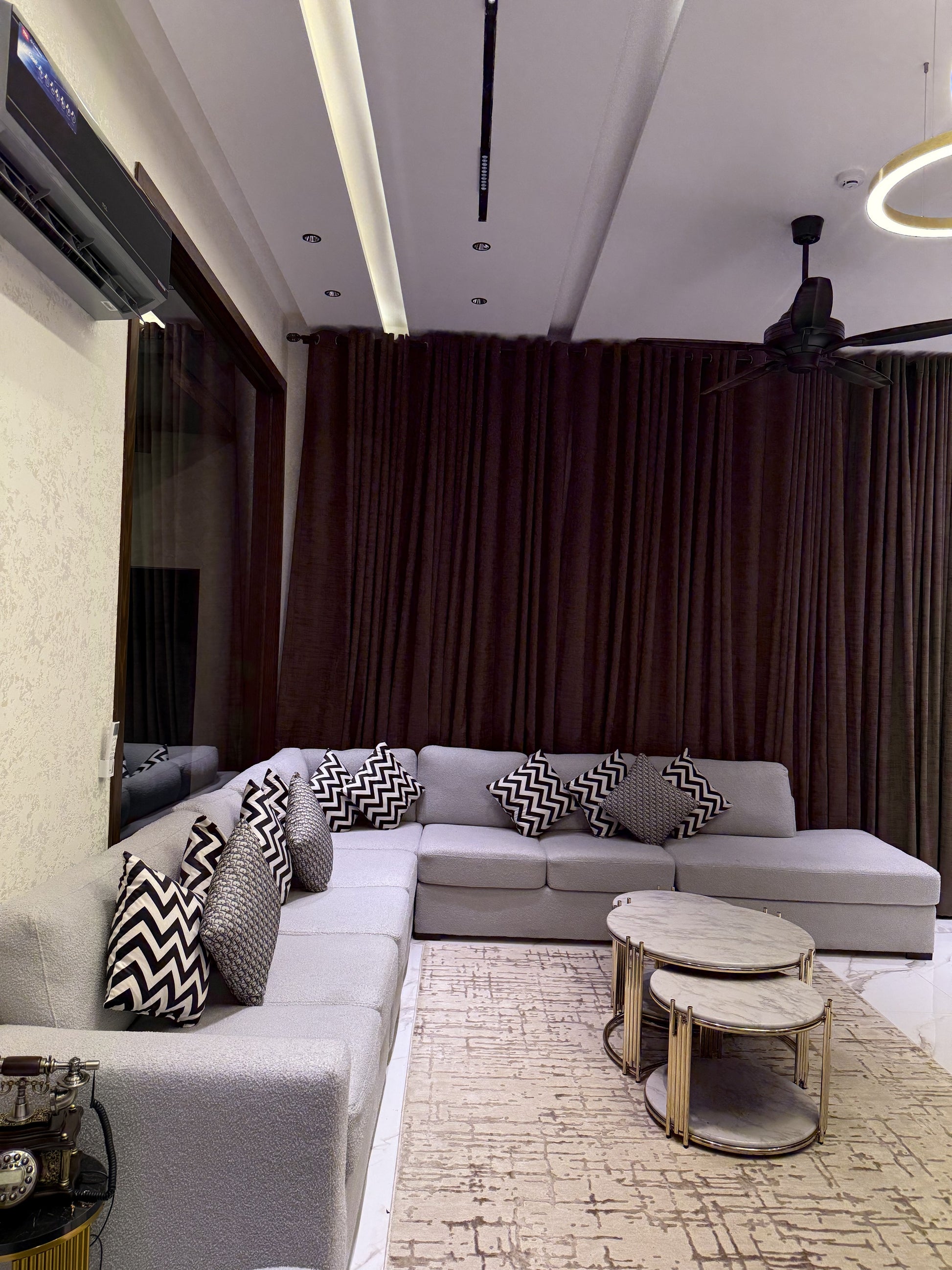 A modern and elegant living room featuring a grey L-shaped sofa and marble-top coffee tables.