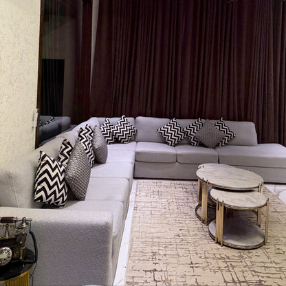 A modern and elegant living room featuring a grey L-shaped sofa and marble-top coffee tables.