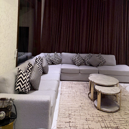 A modern and elegant living room featuring a grey L-shaped sofa and marble-top coffee tables.