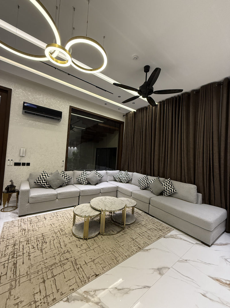 A modern and elegant living room featuring a grey L-shaped sofa and marble-top coffee tables.