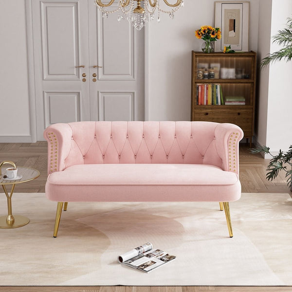 A stylish pink velvet tufted loveseat with gold nailhead trim and gold metallic legs, 
