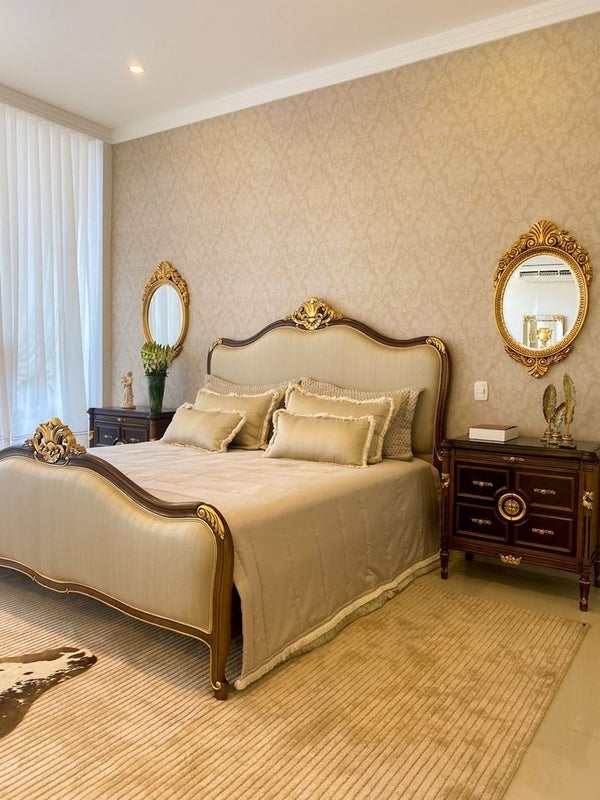 A lavish Louis style bed with a dark wood frame and ornate gold carvings on the headboard and footboard, upholstered in a light beige fabric.