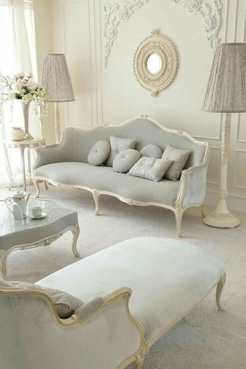 A grand Venetian-style sofa with an ornate c
arved frame and light gray upholstery, accompanied by matching throw pillows,