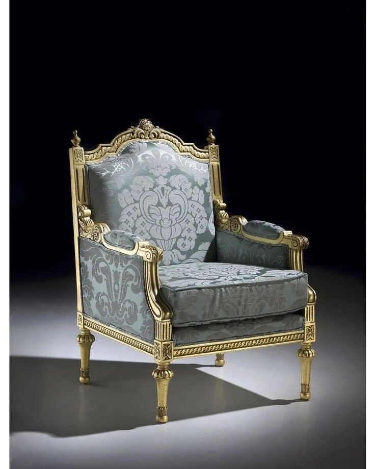 A highly ornate French Louis XV style armchair with a gilded gold carved wooden frame and upholstered in a luxurious blue and grey patterned damask fabric,