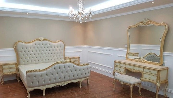 A grand French-style bedroom set featuring a tufted bed with an ornate gold frame, two matching bedside tables, and a dressing table with a mirror and stool.
