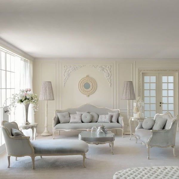 A set of elegant French classical living room furniture, including a grey upholstered sofa, armchair, and chaise lounge with ornate white carved frames, a mirrored coffee table, and a decorative side table.